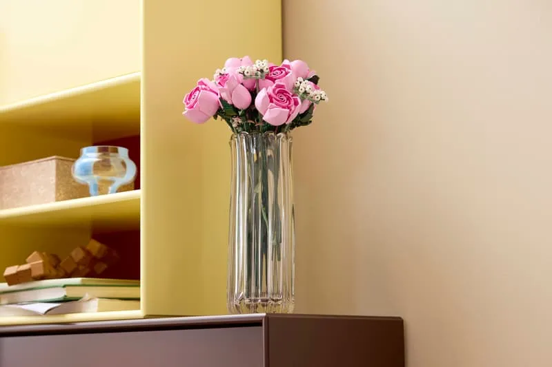 LEGO Bouquet of Pink Roses in a clear vase on a shelf next to a yellow cabinet.