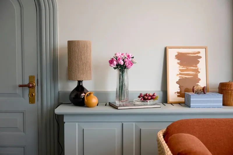 LEGO Bouquet of Pink Roses in a vase on a light blue console table, next to a lamp and framed art.