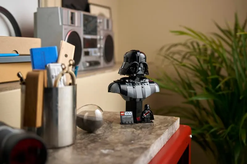 The Lego Darth Vader Bust 75439 displayed elegantly on a shelf in a modern room, alongside other decorative items like a boombox and plants, showcasing its suitability as a home decor piece.