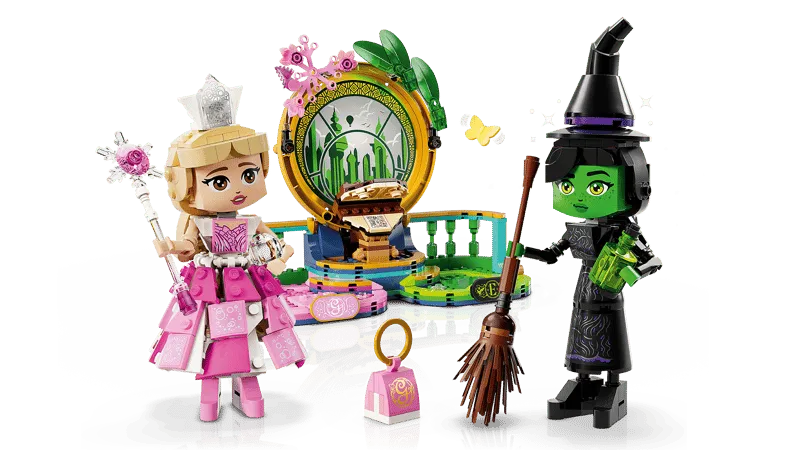 Lego Elphaba and Glinda figures with the Emerald City backdrop and various accessories, including a potion bottle, spellbook, wand, broom, witch hat, and handbag, on a white background.