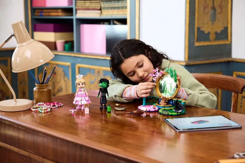 A young girl with long dark hair concentrating while adding a decorative element to the central Emerald City backdrop of the Lego Elphaba & Glinda Figures set.