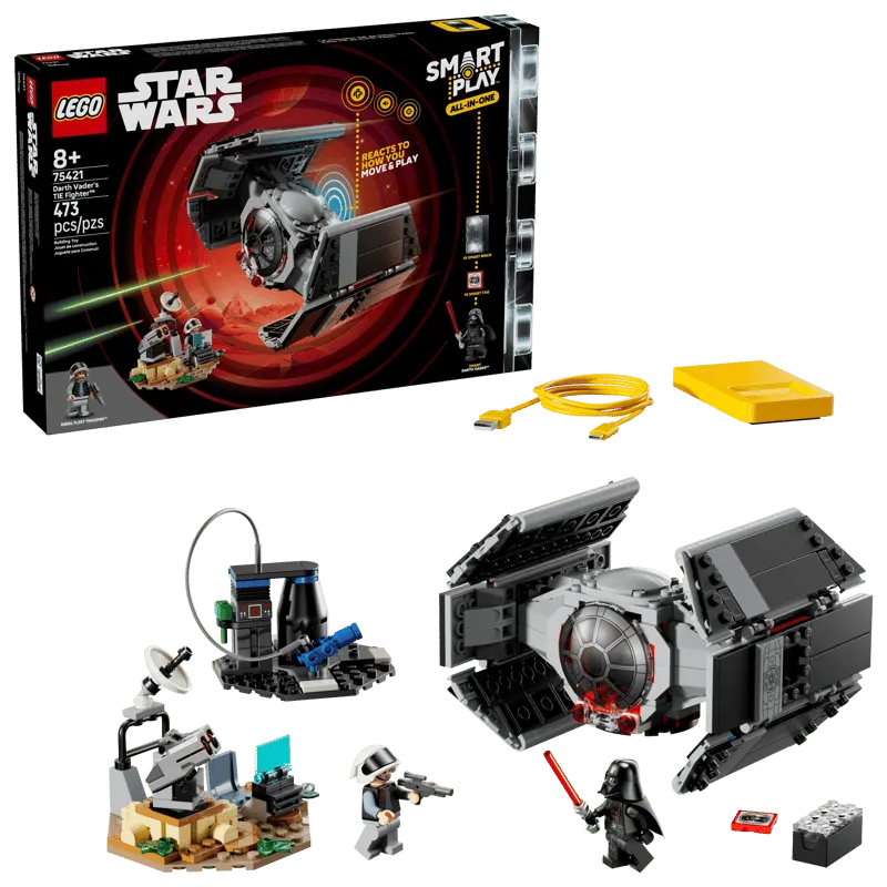 An overhead view displaying the contents of the LEGO Star Wars 75421 set, including the product box, the built Darth Vader's TIE Fighter, a Rebel defense turret, Darth Vader and Rebel Fleet Trooper minifigures, a yellow Smart Charger, a Smart Tag, and a Smart Brick with its connecting cable.