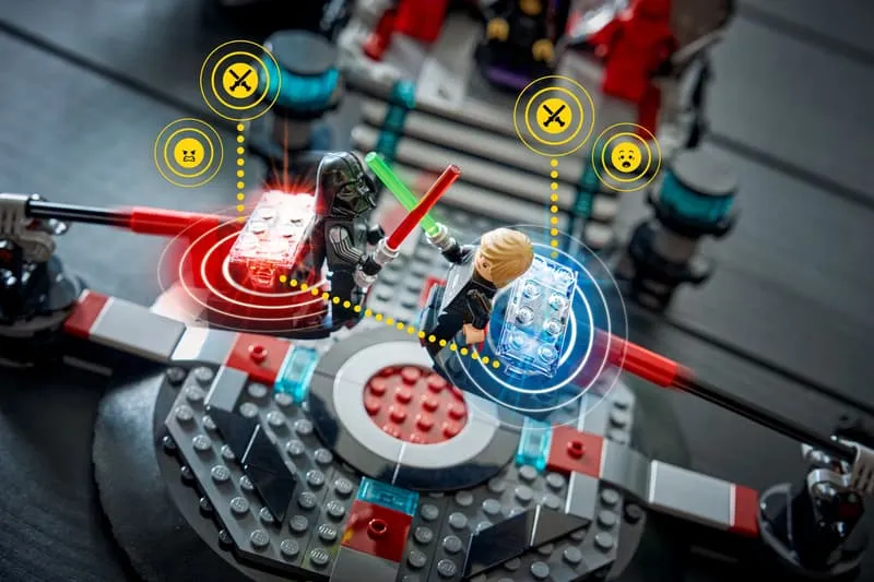 Close-up of Luke Skywalker and Darth Vader minifigures dueling with lightsabers on the movable platforms of LEGO Star Wars 75427, with glowing Smart Play interaction rings and emotional icons above them.