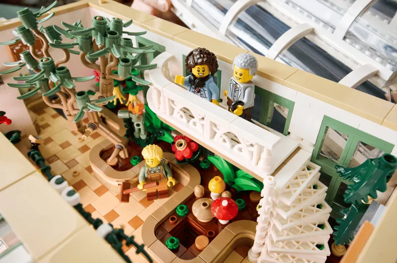 Interior close-up of Lego The Botanical Garden 21353, showing minifigures on an upper balcony overlooking a diverse plant display with a staircase.