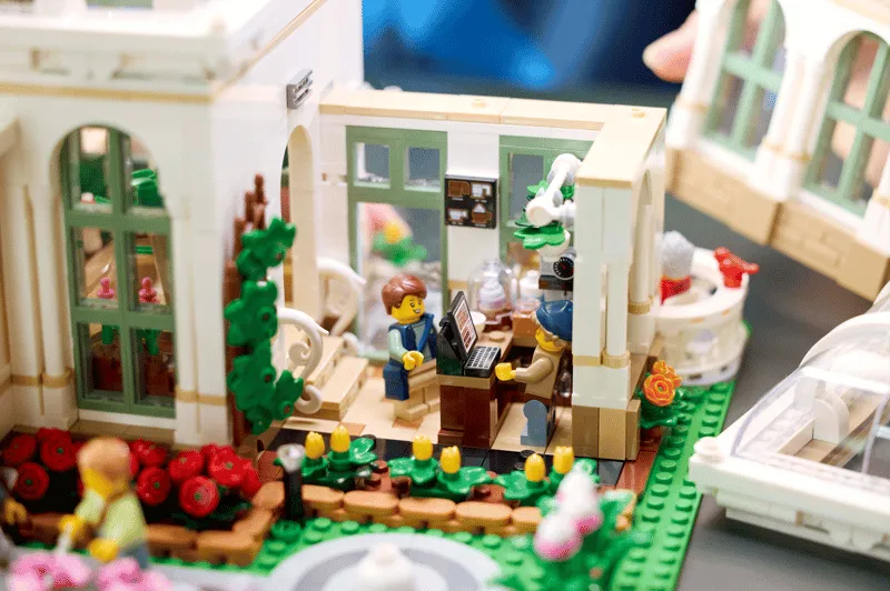 Interior close-up of Lego The Botanical Garden 21353, showing a minifigure at a desk with computers and another tending to plants.