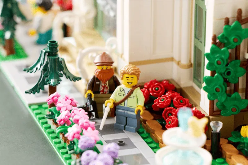 Exterior close-up of Lego The Botanical Garden 21353, showing minifigures on a garden path surrounded by colorful flowers and a fountain.