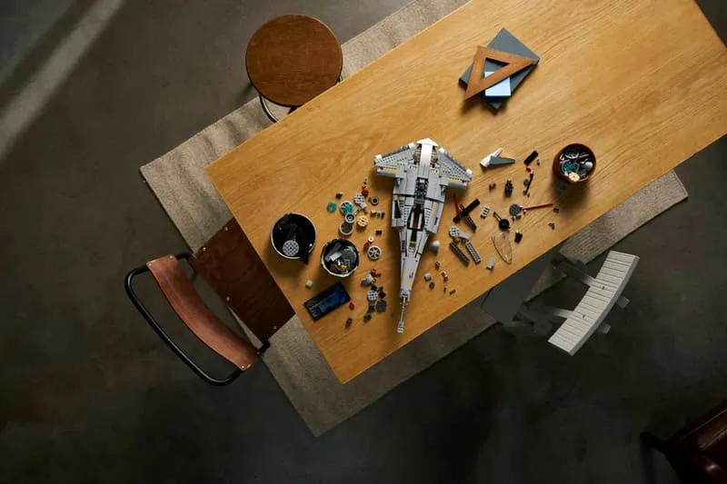 Overhead shot of the Lego N-1 Starfighter UCS set being built on a wooden table, with scattered bricks and components around the partially assembled model.