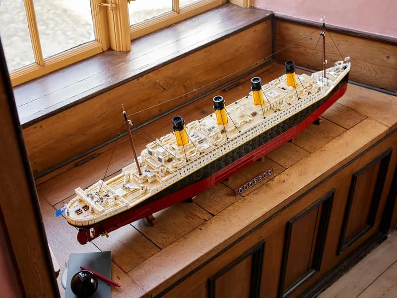 Lifestyle shot of the fully assembled LEGO Titanic model displayed on a wooden surface by a window, showcasing its grandeur in a home setting.