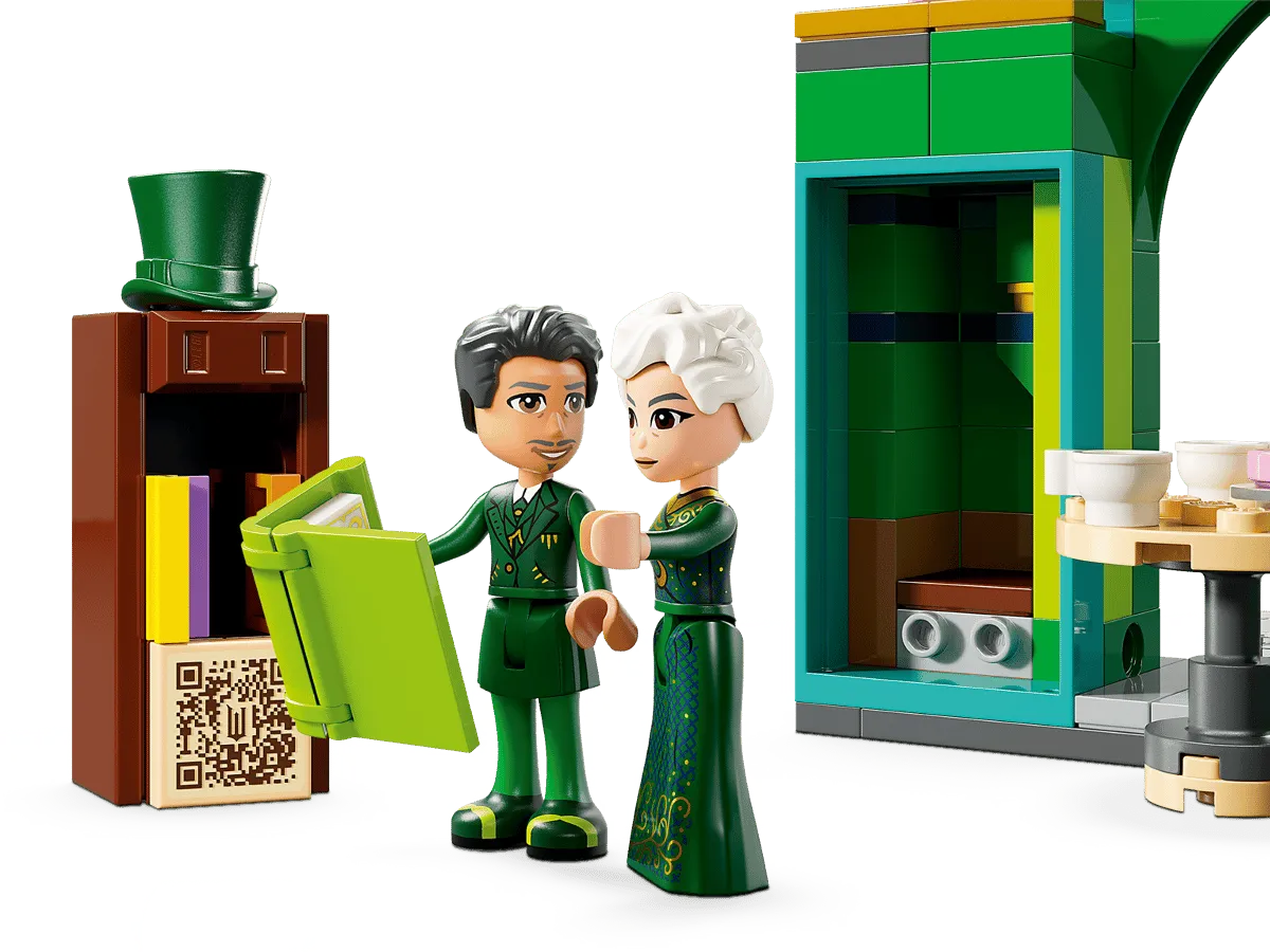 Close-up of two Lego minifigures, a male character and a female character in a green dress (Madame Morrible), reading a large green book near a small brown bookshelf topped with a green top hat.