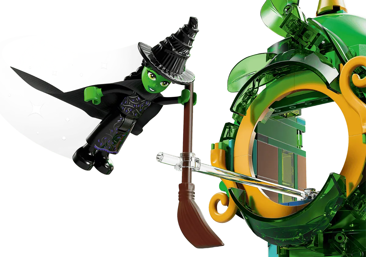 Close-up of the Lego Elphaba minifigure, the Wicked Witch of the West, flying dynamically on her broomstick with a transparent support rod, soaring near the top of the Emerald City tower.