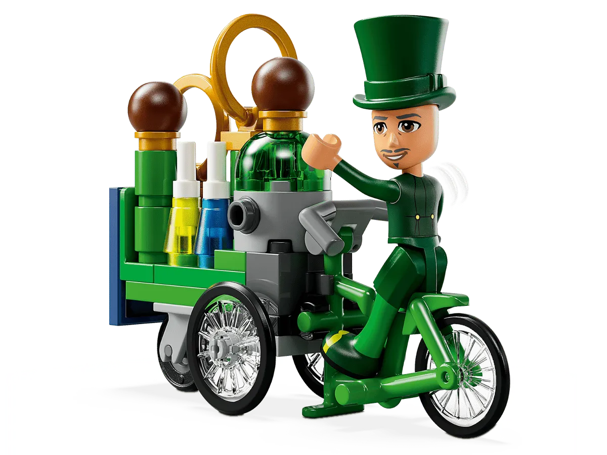 Close-up of a Lego minifigure in a green suit and top hat, cycling a detailed green tricycle that carries various bottles and other small accessories, against a plain white background.