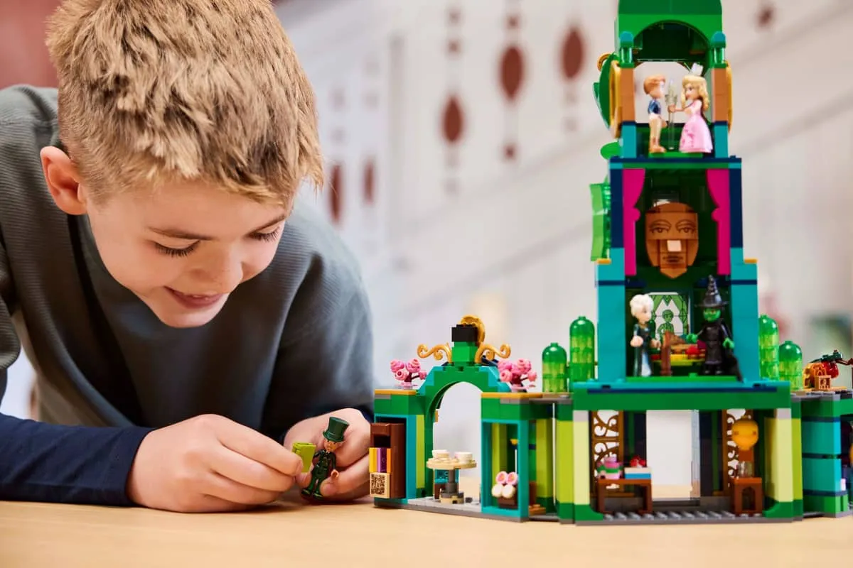 Close-up of a boy smiling and focusing intensely while playing with the Lego Welcome to Emerald City 75684 set, specifically arranging a minifigure near the lower level of the green tower.