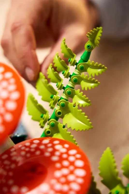 A hand holding one of the vibrant green fern sub-assemblies from the LEGO Woodland Mushrooms set, demonstrating its articulated structure and the details of its serrated leaves.